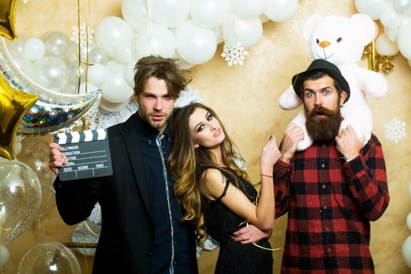 Sensual woman and men in movie or film studio. Boyfriends with movie clapper and teddy bear toy. Cinema theme party for holiday celebration. Lovers celebrate christmas or new year, love triangle.